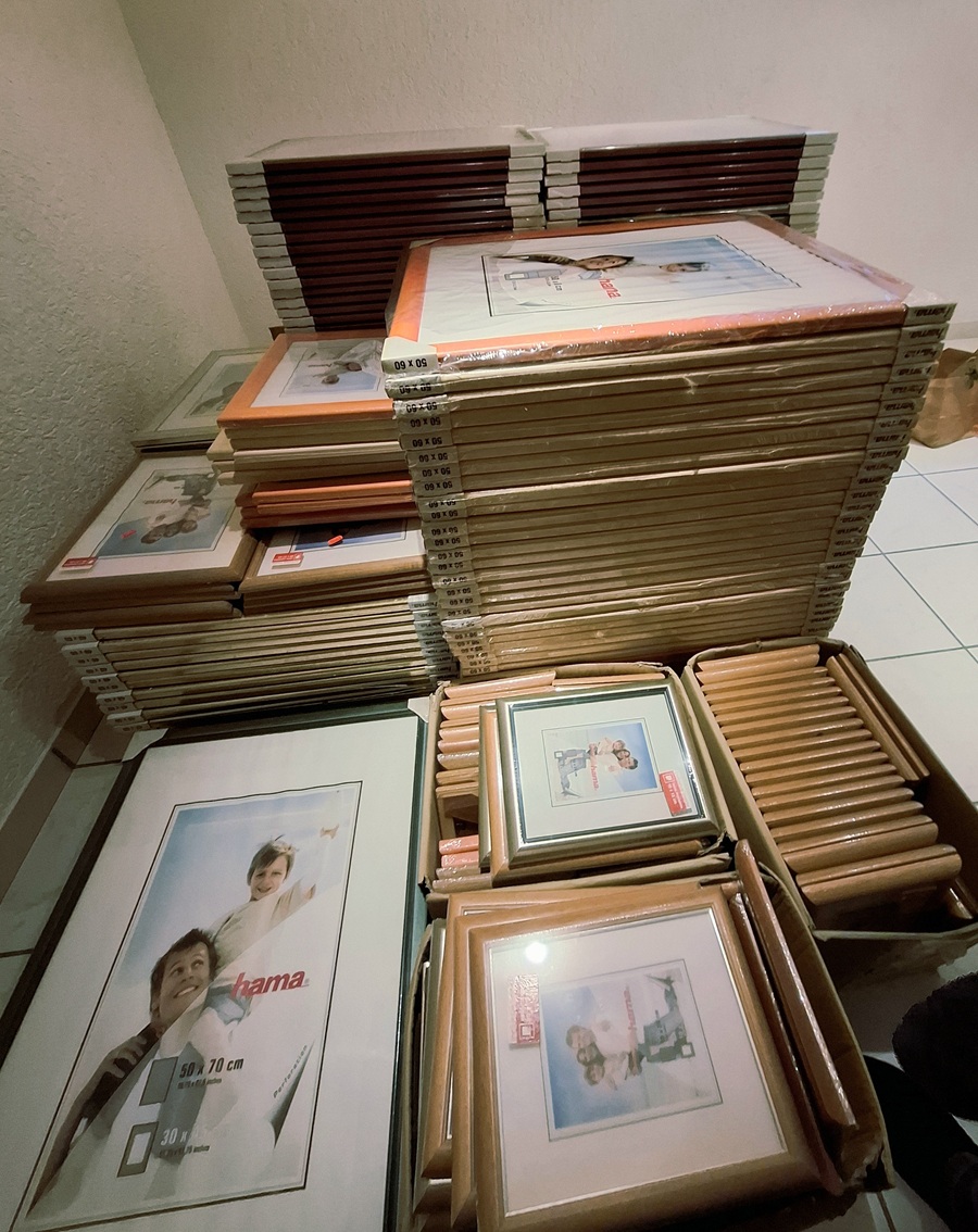 Von schräg oben fotografiert die Draufsicht verschiedener Stapel unterschiedlich großer Bilderrahmen, im Vordergrund sind kleinere Holzrahmen in Kartons zu sehen.