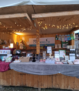 Ein Weihnachtsmarktstand mit diversen Waren mit Tiermotiven. Er ist schön beleuchtet, im Hintergrund ein Banner mit der Aufschrift "Gitte Härter" und meinem Logo.