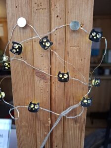 Eine Lichterkette mit kleinen Katzenköpfen ist mit Reißnägeln an einem Holzpfosten befestigt.